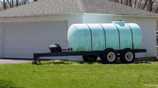 Plastic tank on wheels in front of a white house.