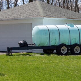 Plastic tank on wheels in front of a white house.