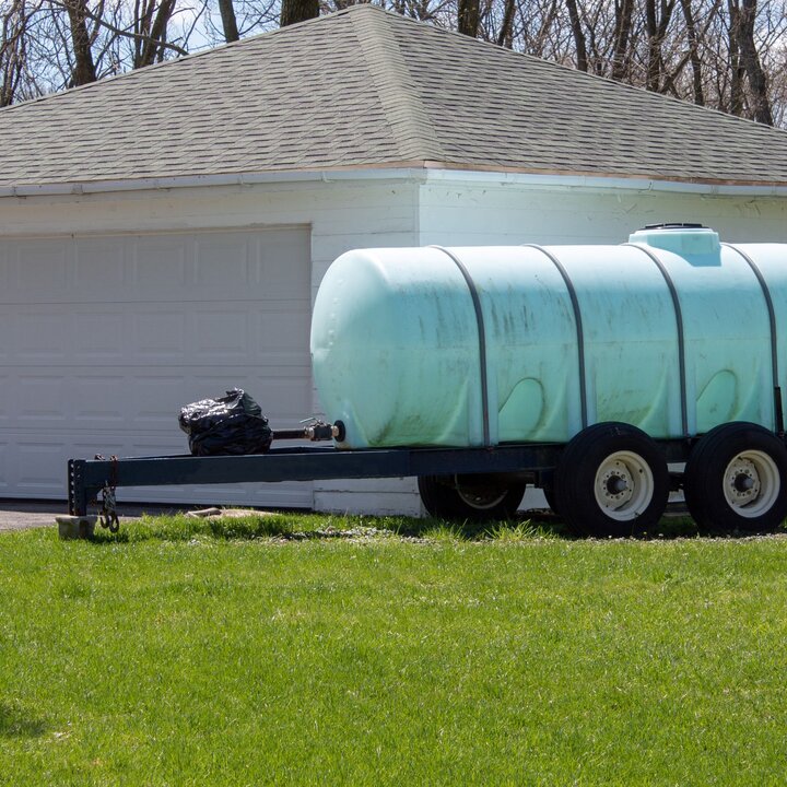 Plastic tank on wheels in front of a white house.