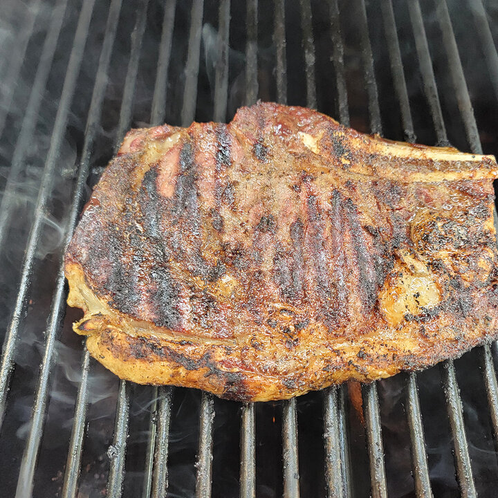 Grilled beef steak with char marks on a smoky black grill.